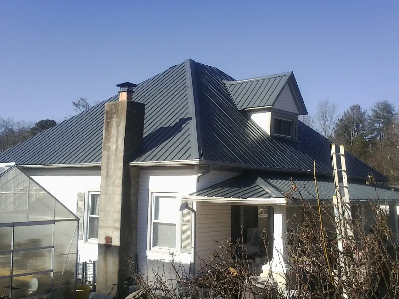 Dark blue standing seam metal roof on a white farmhouse with dormer — Slate & Tile Roof Repair by Roofing Brothers in Little Neck