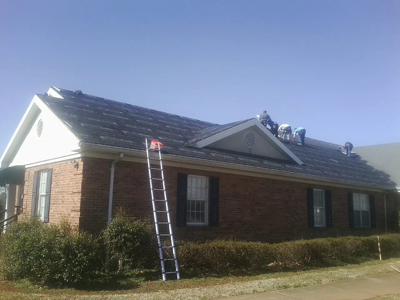 Crew tearing shingles off a brick ranch roof with a ladder set — Metal Roof Repair work by our crew in Little Neck