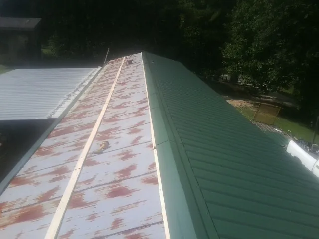 Old rusted panels beside newly installed green metal roofing — Wind Damage Roof Repair by Roofing Brothers in Little Neck