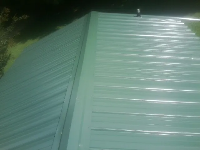 New green metal panels meeting at the ridge of a roof — Flat Roof Repair work by our crew in Little Neck