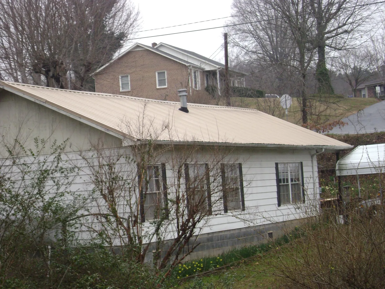 Tan metal roof on a white sided house set into a hillside — Commercial Roofing by Roofing Brothers in Little Neck