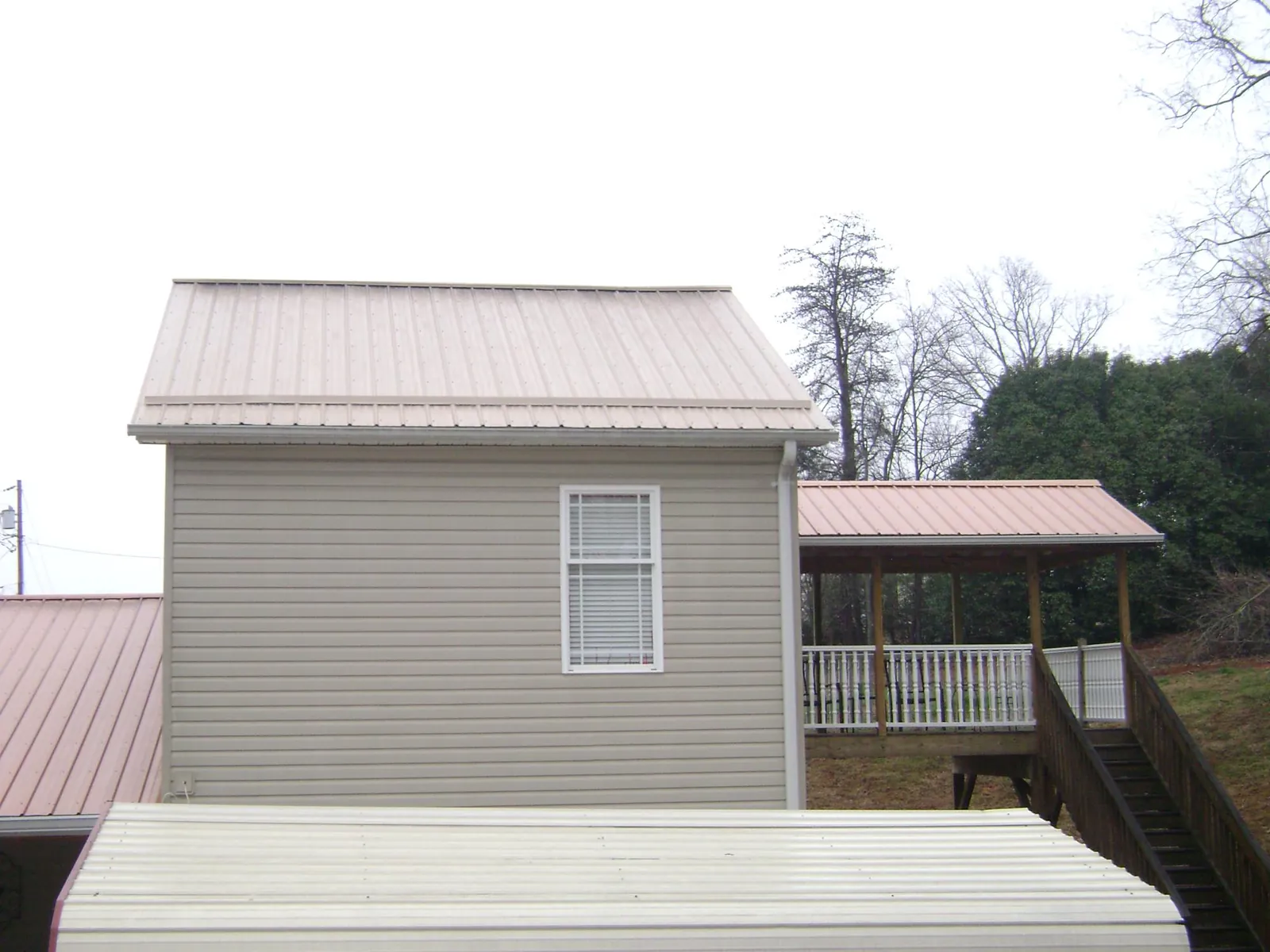 Tan metal roofs on a two story addition and attached porch, from a Roof Replacement job in Little Neck